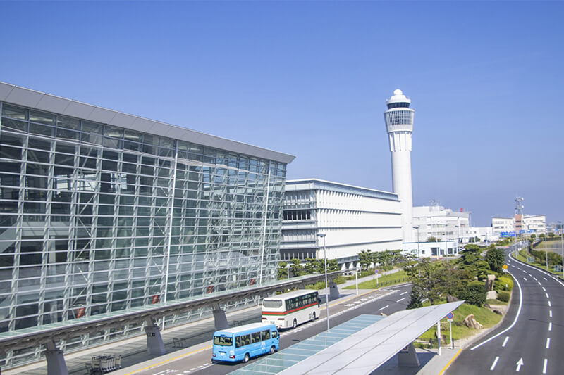 空港の外観と道路、送迎バスが並ぶ出発エリアの風景。